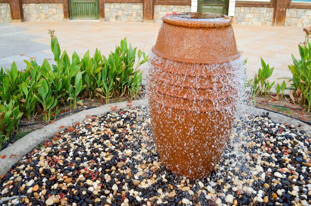 Ein schöner kleiner Brunnen in Form einer braunen Vase auf einem Krug mit fallenden Wassertropfen auf farbig