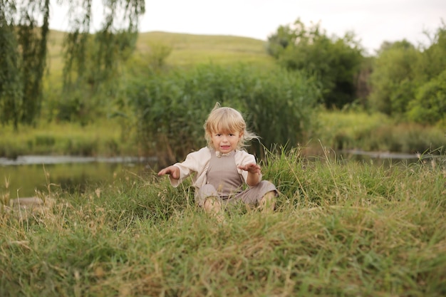 Ein schöner kleiner Junge mit blonden Haaren und lockigem Haar ruht in der Natur am Fluss