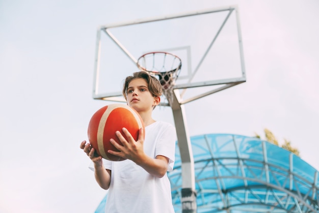 Foto ein schöner teenager in einem weißen t-shirt steht auf dem basketballplatz und hält einen basketball
