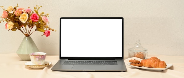 Ein schöner weiblicher Arbeitsplatz mit einem Computerbildschirm-Modell, einer Blumenvase, einer Kaffeetasse und Gebäck.