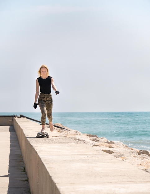 Ein schönes blondes Mädchen auf Skateboard im heißen Sommertag am Meer