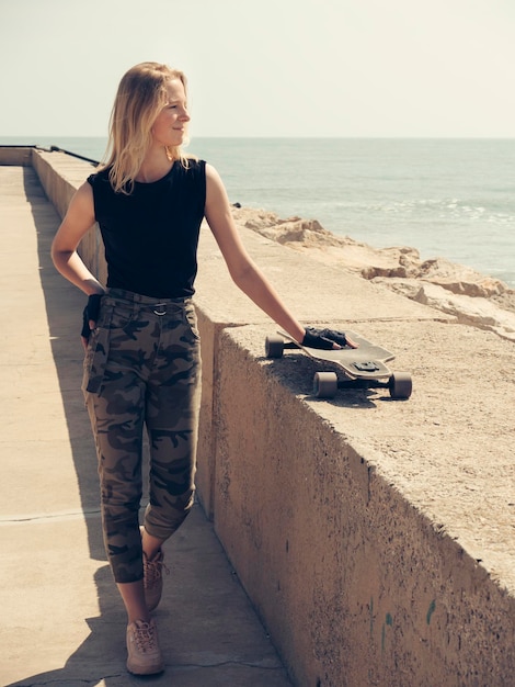 Ein schönes blondes Mädchen geht auf den Pier und schiebt die Skatehand