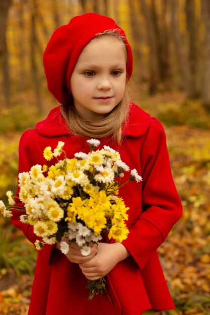 Ein schönes blondes Mädchen in rotem Mantel und Baskenmütze hält einen Strauß Herbstblumen in den Händen