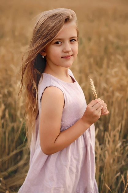 ein schönes blondes mädchen mit langen haaren in einem leinenrosa kleid steht auf einem weizenfeld sommer