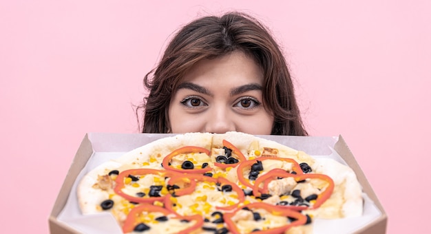 Ein schönes brünettes Mädchen mit großen Augen schaut aus einer Pizzaschachtel.