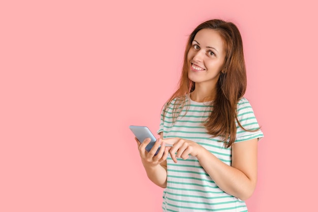 Ein schönes brünettes Mädchen wählt eine Telefonnummer auf einem Smartphone. Porträt einer Frau auf rosa Hintergrund mit einem Handy.