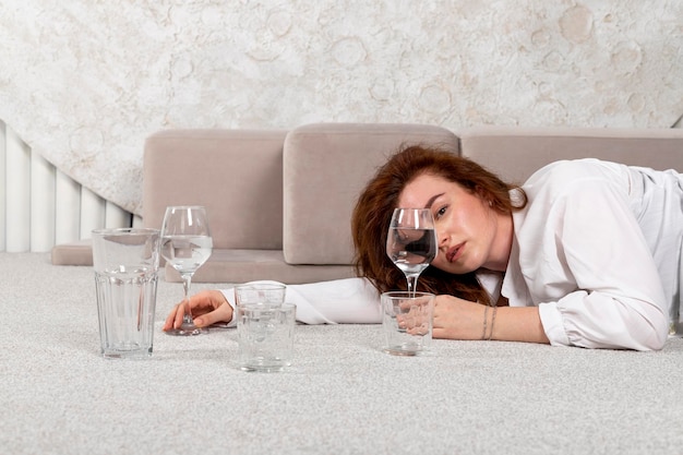 Foto ein schönes, gesundes brünettes mädchen hält ein glas wasser oder eine klare flüssigkeit auf dem boden und demonstriert das produkt vitamine, die feuchtigkeit spenden, getränke und alkohol