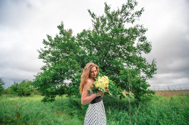 Ein schönes junges blondes Mädchen sammelte einen Strauß Wildblumen. Genießen Sie einen Spaziergang an einem warmen Sommertag.