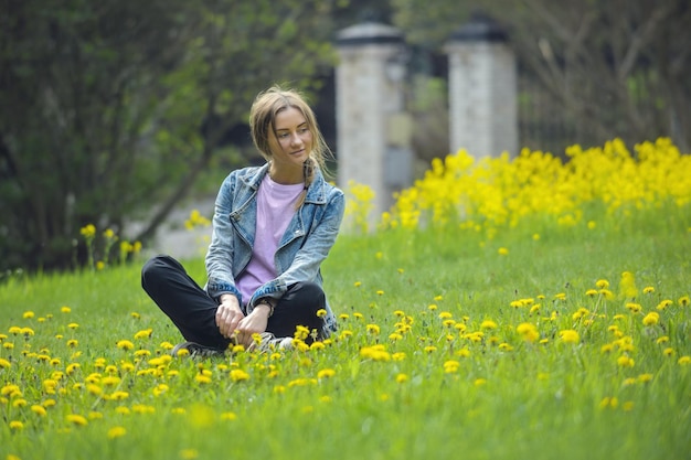 Ein schönes junges Mädchen auf einem Spaziergang sitzt auf einer hellgrünen Wiese mit gelben Blumen