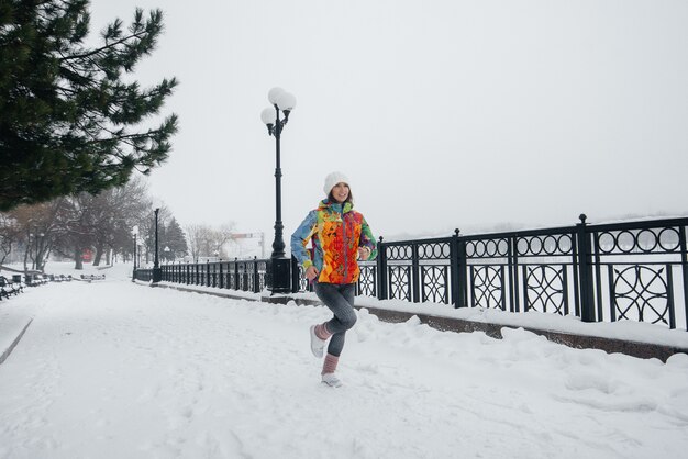 Ein schönes junges Mädchen joggt an einem frostigen und schneereichen Tag. Sport, gesunder Lebensstil