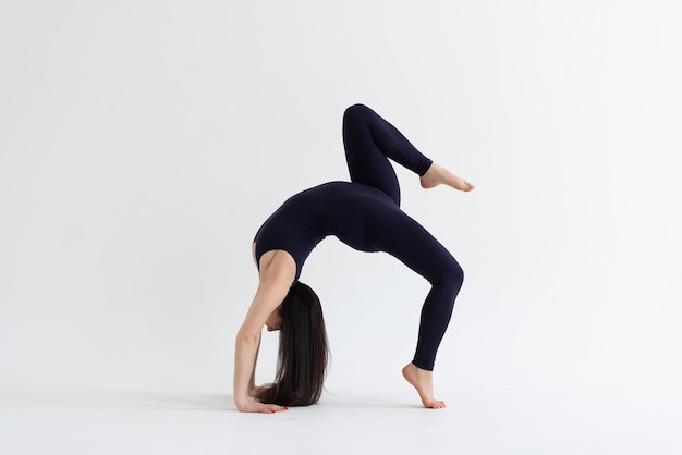 Ein schönes junges Mädchen mit dunklem Haar steht in der Pose von Eka Pada Urdhva Dhanurasana Variation