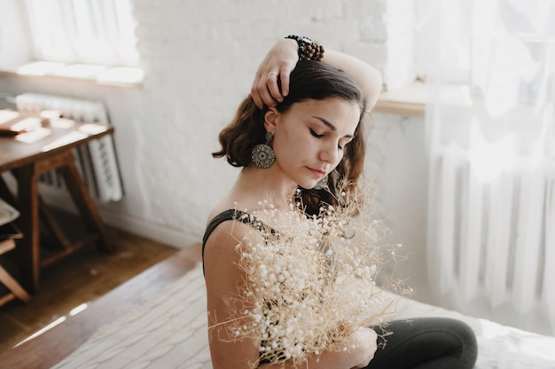 Ein schönes junges Mädchen mit einem Strauß weißer Blumen sitzt mit geschlossenen Augen auf dem Bett ja