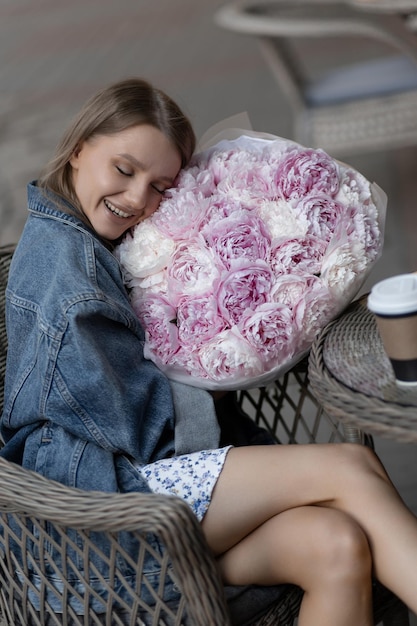 Foto ein schönes kaukasisches mädchen in einem lässigen outfit sitzt in einem straßencafé mit einem strauß schöner pfingstrosen in ihren händen