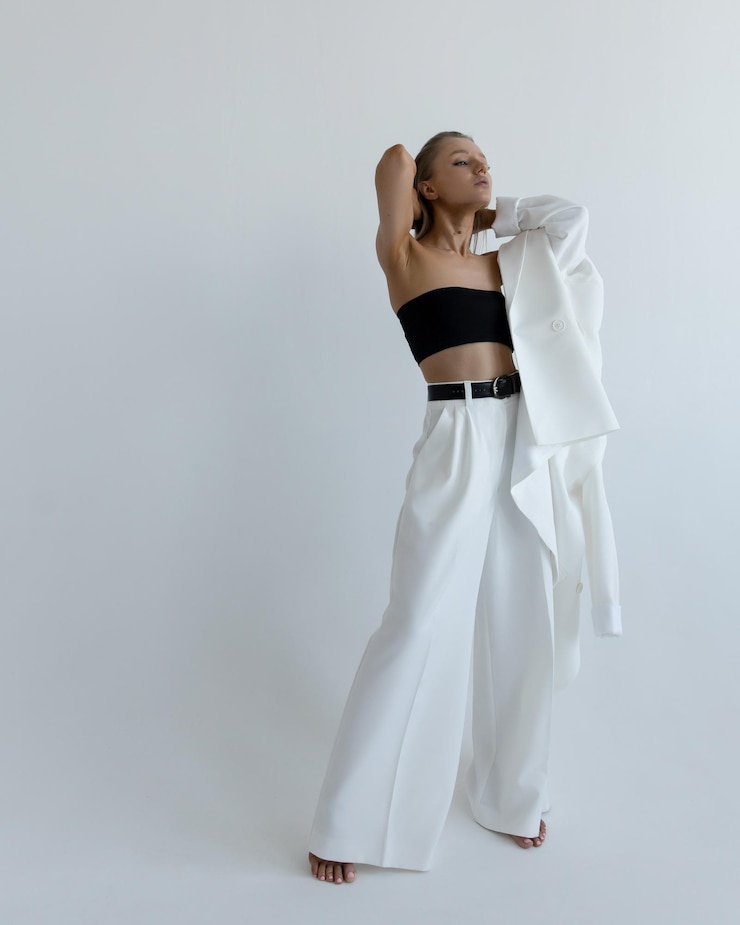 Foto ein schönes kaukasisches mädchen in einem weißen anzug steht in einer modischen pose in einem studio auf weißem hintergrund und zieht es aus