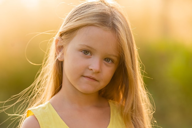 ein schönes kleines Mädchen mit langen blonden Haaren geht im Sommer bei Sonnenuntergang im Stadtpark spazieren