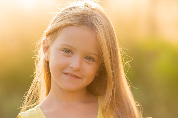 ein schönes kleines Mädchen mit langen blonden Haaren geht im Sommer bei Sonnenuntergang im Stadtpark spazieren