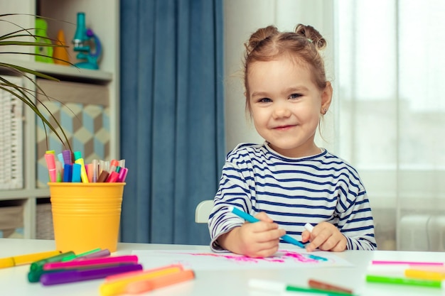 Ein schönes kleines Mädchen sitzt zu Hause an einem Tisch und zeichnet Entwicklung von Vorschulkindern