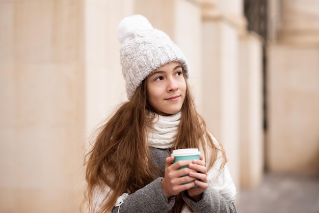 Ein schönes lächelndes Mädchen mit einer Tasse Kaffee geht durch die Stadt Winter-Herbst-Atmosphäre