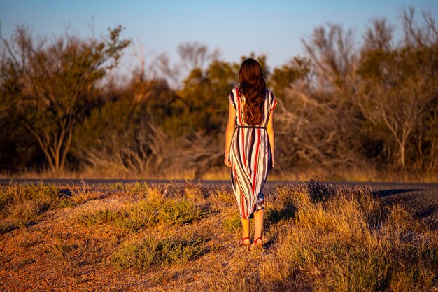 ein schönes langhaariges mädchen in einem langen kleid geht entlang einer straße in der wüste in westaustralien