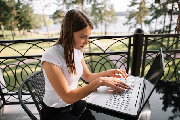 Ein schönes Mädchen arbeitet an einem Sommertag mit ihrem Laptop auf dem Balkon.