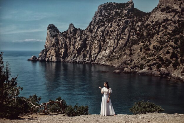 Ein schönes Mädchen, eine Braut in einem weißen Kleid steht auf einer Klippe