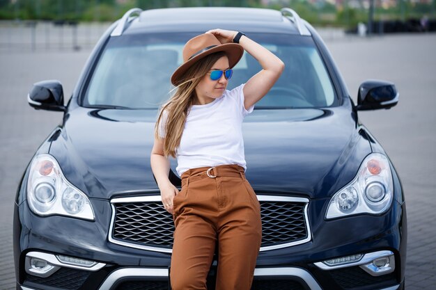 Foto ein schönes mädchen europäischen aussehens mit brille und braunem hut steht in der nähe eines schwarzen autos.