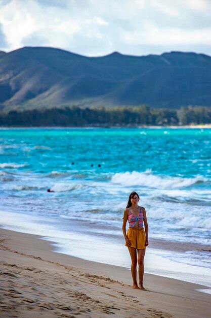 Ein schönes Mädchen geht an einem paradiesischen Strand auf der hawaiianischen Insel Oahu mit Blick auf die Berge spazieren