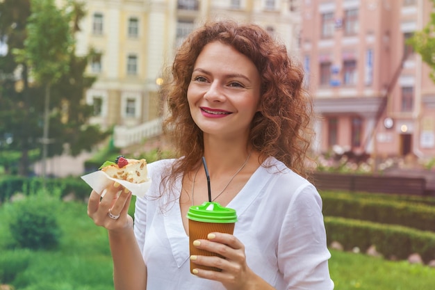 Ein schönes Mädchen im Park trinkt eine Kaffeetasse aus einem Pappbecher durch einen Strohhalm und hält