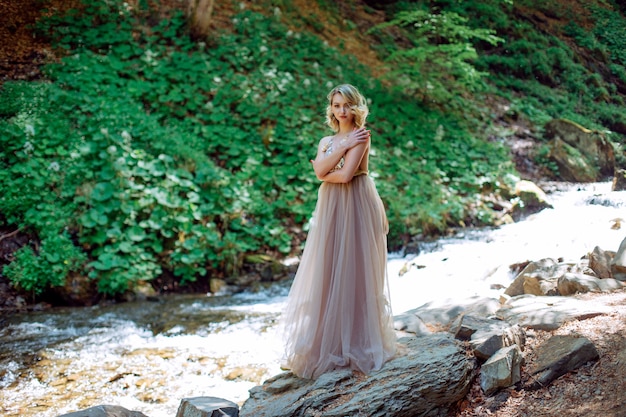 Ein schönes Mädchen in einem Kleid steht nahe dem Flussbett in der Natur im Freien