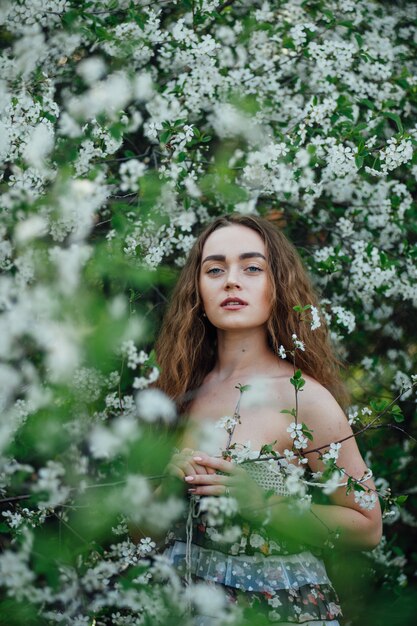 Ein schönes Mädchen in einem Kleid steht neben einem blühenden Kirschbus