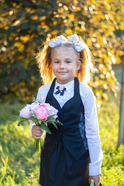 Ein schönes Mädchen in einer Schuluniform mit weißen Schleifen geht in die 1. Klasse