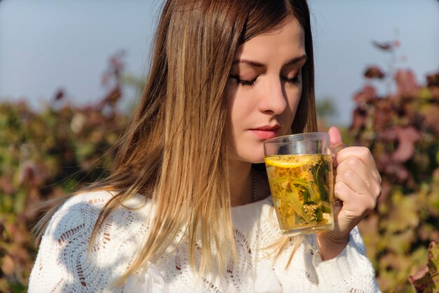 Ein schönes Mädchen in einer weißen Strickjacke trinkt den heißen im Freientee