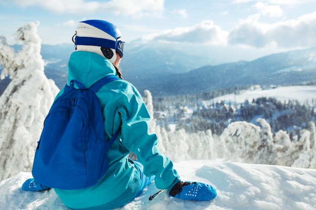 Ein schönes Mädchen in Winterkleidung, einem blauen Helm und einer grünen Jacke hat eine tolle Zeit in den Bergen.