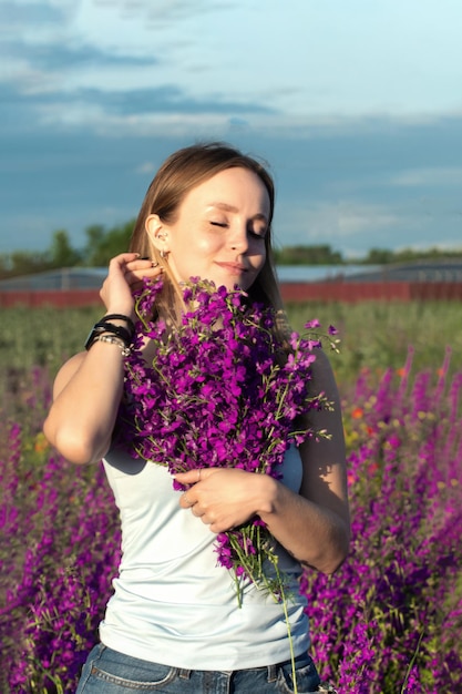 ein schönes mädchen mit blonden haaren hält einen blumenstrauß aus helllila feldblumen in ihren händen