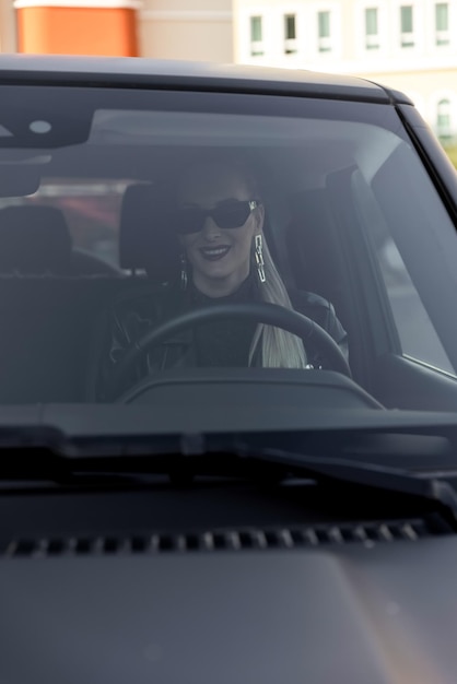 Ein schönes Mädchen mit blonden Haaren mit einem großen schwarzen Auto in einem Kleid mit offenem Rücken. Lange Haare u