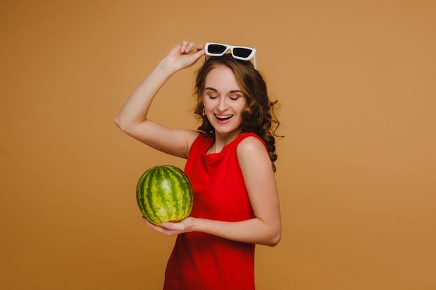 Ein schönes Mädchen mit Brille und rotem Kleid hält eine Wassermelone in den Händen