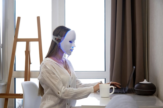Foto ein schönes mädchen mit einer led-maske auf dem kopf arbeitet an einem laptop