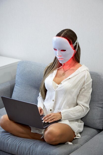 Foto ein schönes mädchen mit einer led-maske auf dem kopf arbeitet zu hause an einem laptop