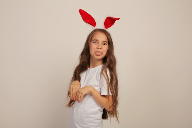 ein schönes Mädchen mit langen Haaren in einem weißen T-Shirt mit Hasenohren lächelt Ostern