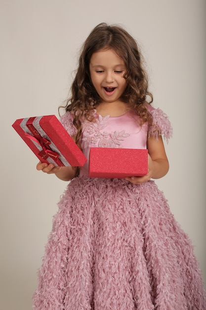 Ein schönes Mädchen mit lockigem Haar in einem rosa Kleid mit einer Geschenkbox in den Händen ist ein Feiertag