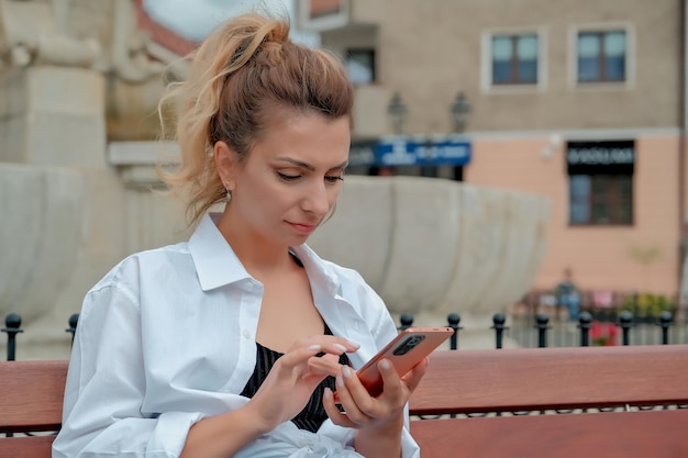 Ein schönes Mädchen sitzt auf einer Bank und hält ein Telefon in den Händen. Das Mädchen bestellt Essen durch