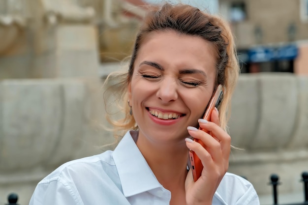 Ein schönes mädchen sitzt auf einer bank und hält ein telefon in ihren händen das mädchen bestellt essen über das telefon das mädchen spricht am telefon und lacht glücklich überrascht