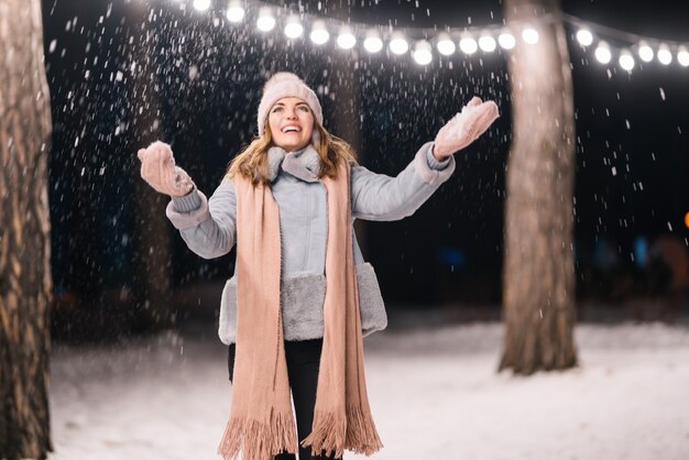 Ein schönes Mädchen spielt mit Schnee Fröhliche Winterzeit im Wald Festliche Girlandenlichter