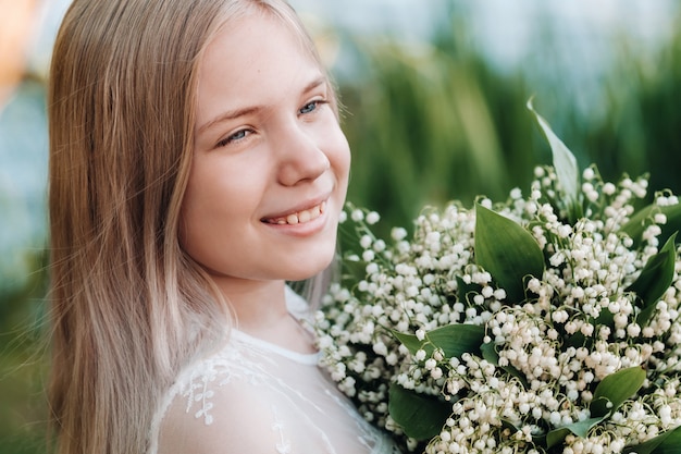 Ein schönes neunjähriges blondes Mädchen mit langen Haaren in einem langen weißen Kleid, das einen Strauß Lilien hält