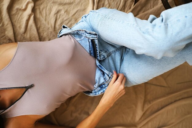 Ein schönes schlankes Mädchen in einer Bodysuit-Jeans liegt auf einem beigen Stoff mit aufgeknöpfter Fliege