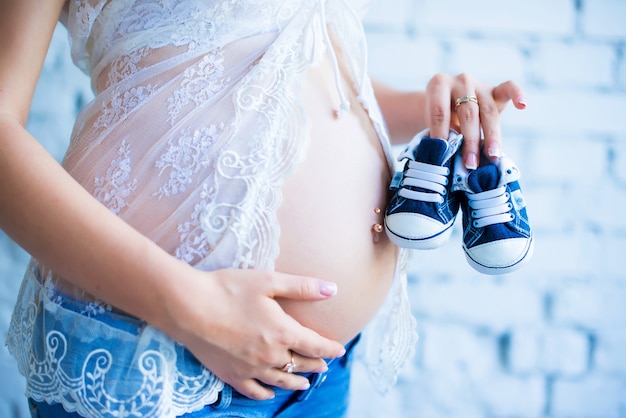 Ein schönes schwangeres Mädchen mit Turnschuhen für Kinder hält in der Nähe des Bauches.