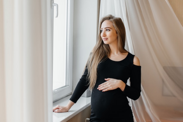 Ein schönes schwangeres Mädchen steht in einem Raum in der Nähe des Fensters