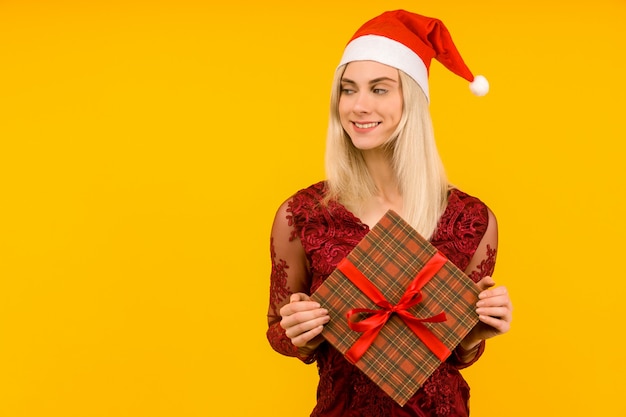 Ein schönes sexy mädchen in einem neujahrshut und einem grauen kleid, halten in den händen geschenke auf gelbem hintergrund. weihnachts- oder neujahrsfeier