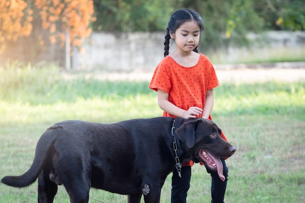 Ein schönes südostasiatisches mädchen in roten outfits spielt abends mit ihrem großen hund im hinter- oder vorgarten. konzept für tierliebhaber