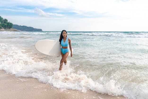 Ein schönes Surfermädchen mit einem schlanken Körper im Bikini und mit Surfbrett, das Spaß am Strand hat.